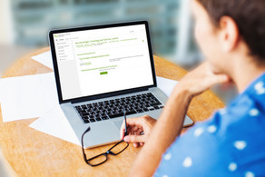 Student sits at workstation and looks at laptop.